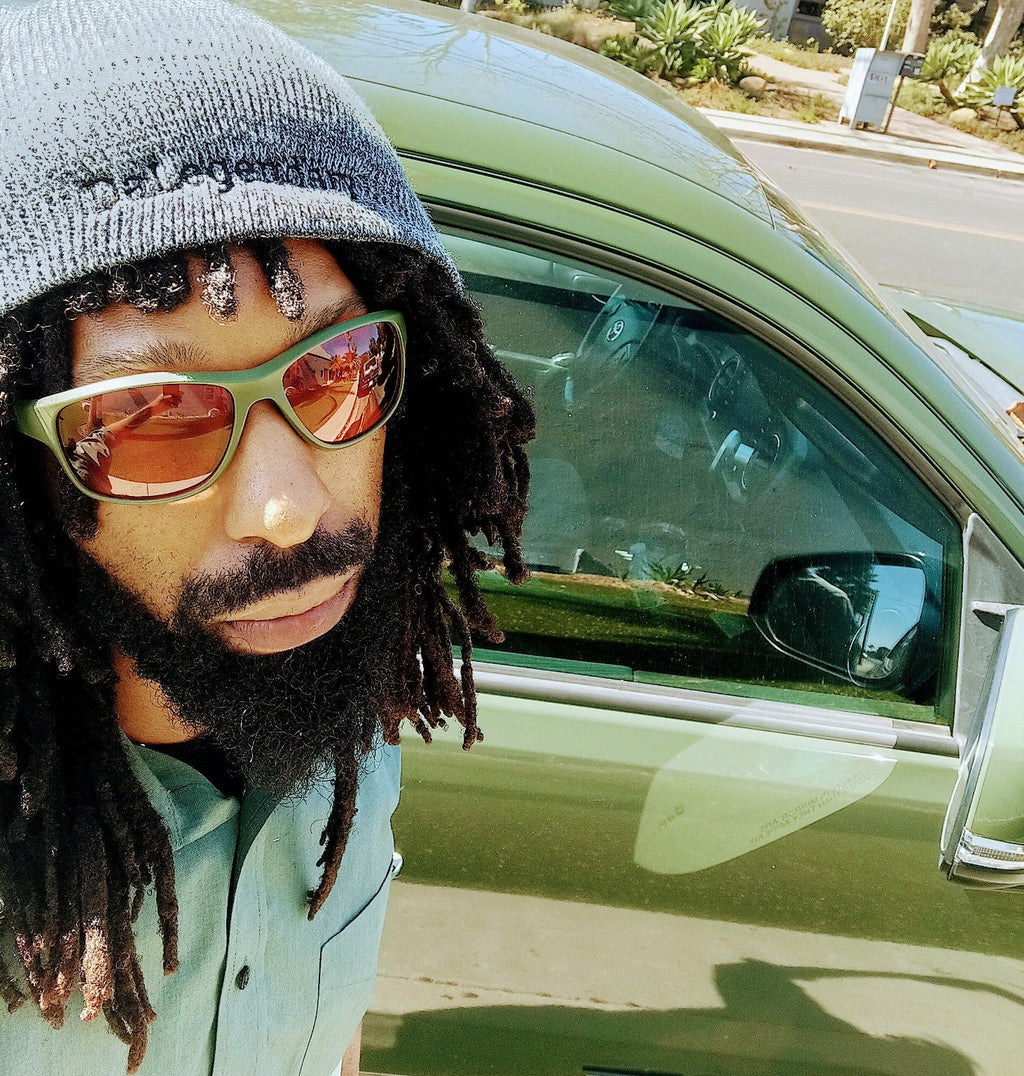Da One Sunset Olive Green sunglasses worn beside an olive green vehicle