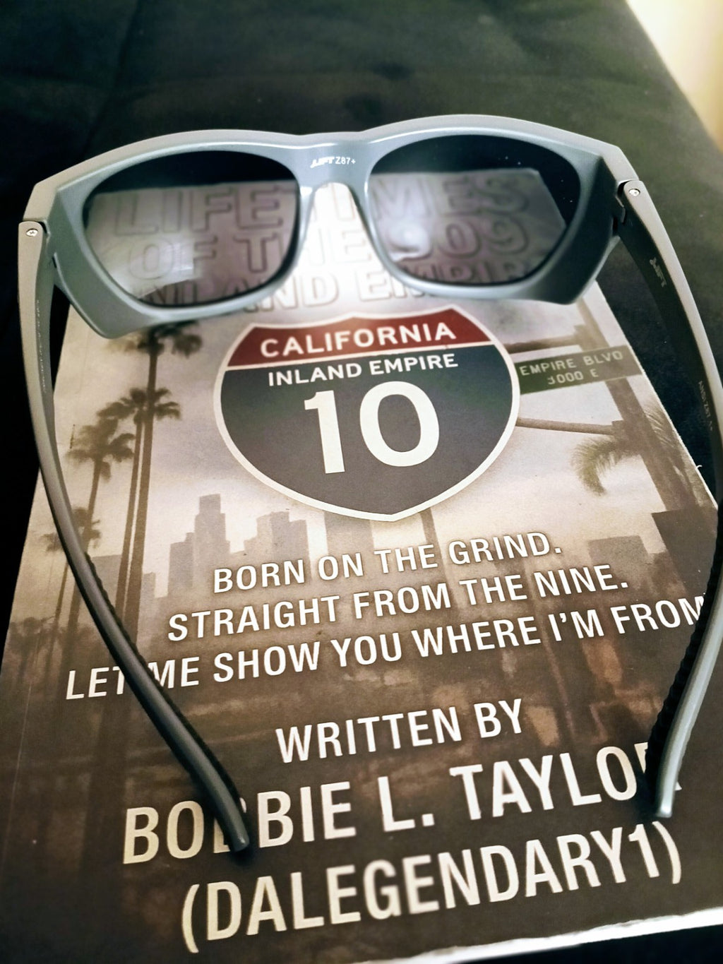 Grey Lift sunglasses resting on Lifetimes of the 909 book, front view. Book sold separately.