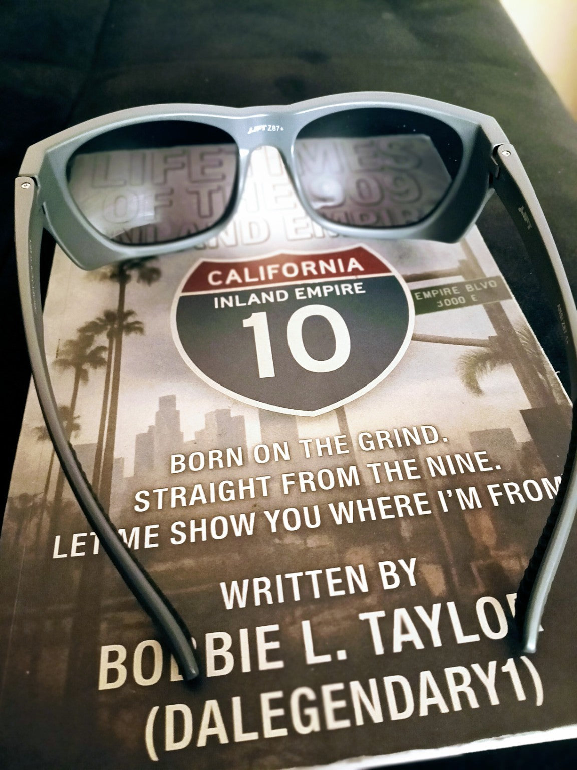 Grey Lift sunglasses resting on Lifetimes of the 909 book, front view. Book sold separately.