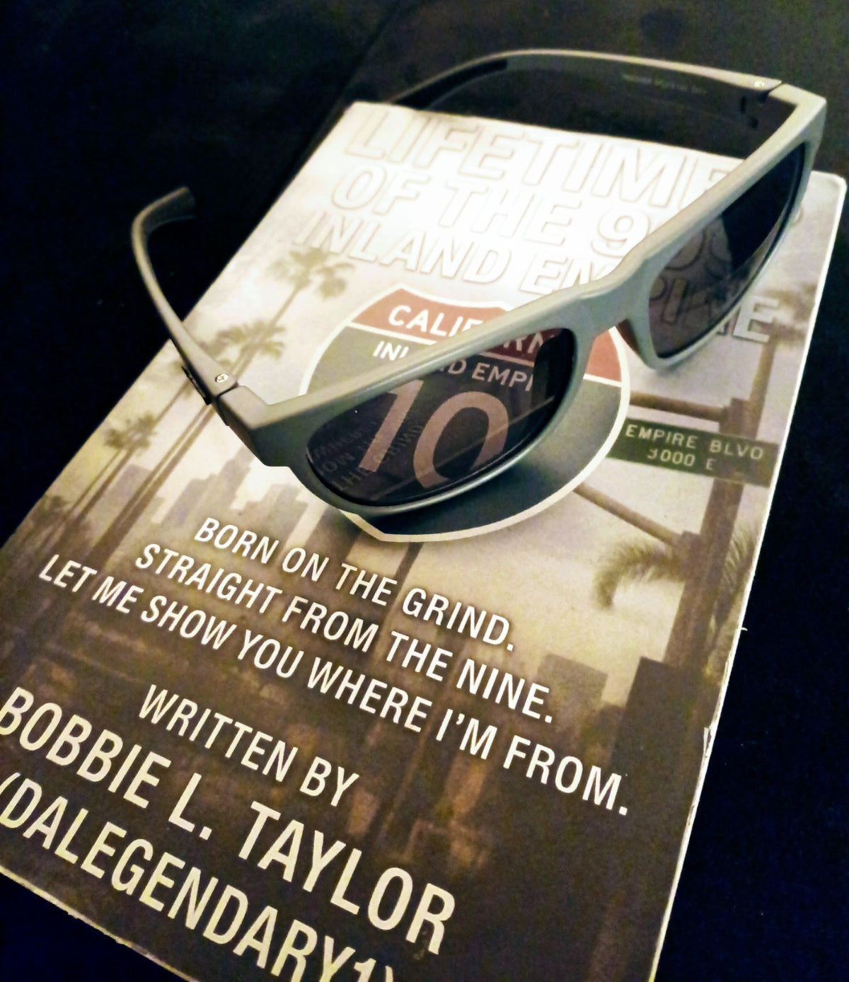Grey Lift sunglasses resting on Lifetimes of the 909 book, angled view. Book sold separately.